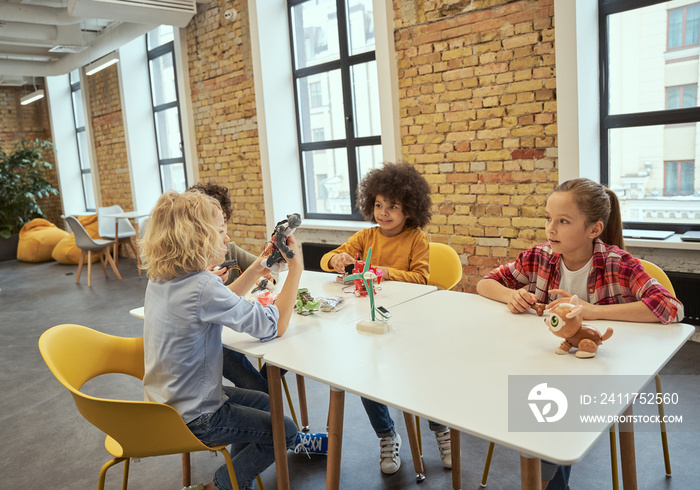 Communication. Group of smart little kids constructing technical toys and making robots while sitting together at the table during STEM class