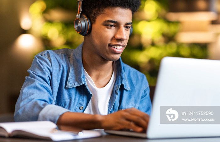 Smiling afro guy in headphones looking at laptop