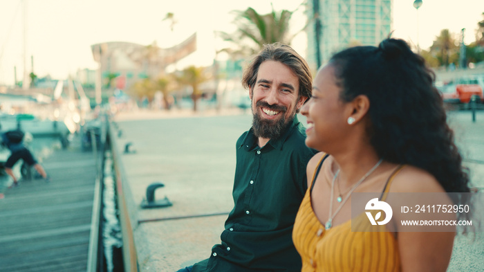 Close-up of happy interracial couple sitting in the port. Closeup, young family talking and smiling in front of passing yachts