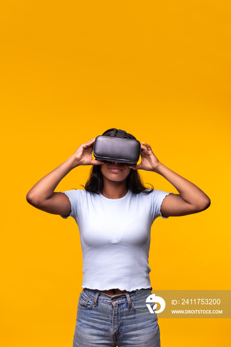 Young woman wearing VR headset on yellow background. Vertical portrait of Asian female wearing virtual reality goggles.