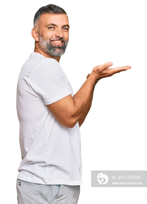 Middle age handsome man wearing casual white tshirt pointing aside with hands open palms showing copy space, presenting advertisement smiling excited happy