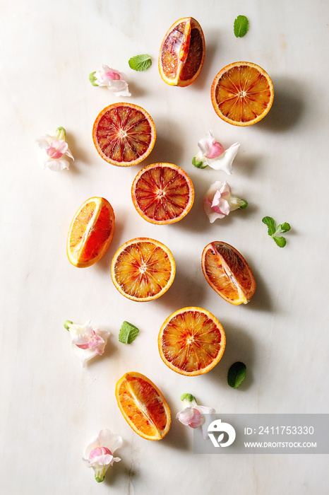 Group of fresh organic Sicilian blood oranges sliced and whole, edible flowers, mint leaves over white marble background. Flat lay, space