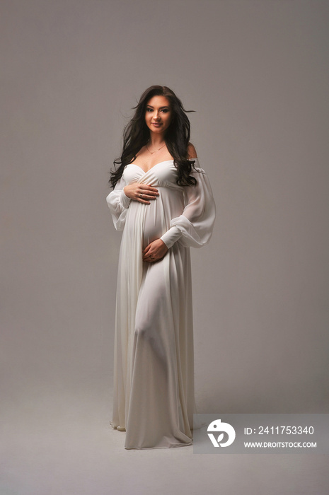 Pregnant brunette woman posing at camera isolated on cyclorama. Expecting baby