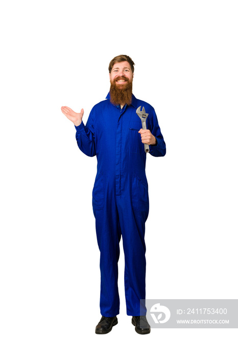 Young adult redhead mechanic man full body isolated showing a copy space on a palm and holding another hand on waist.