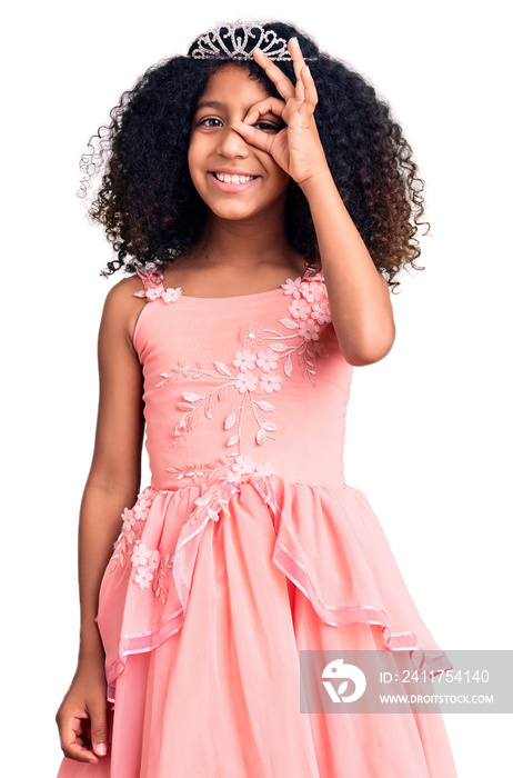 African american child with curly hair wearing princess crown smiling happy doing ok sign with hand on eye looking through fingers