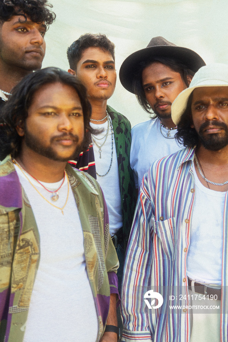 Malaysian Indian men in a group against a cloth backdrop in a park surrounded by trees, talking, laughing and sitting together