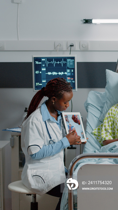 Medic holding tablet with cardiology figure to show diagnosis to woman in bed. Medical physician explaining cardiovascular exam results on device screen to sick patient. Healthcare checkup