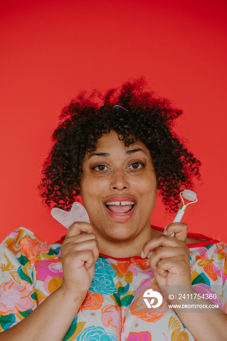 close up of a plus size black person smiling holding skin care tools