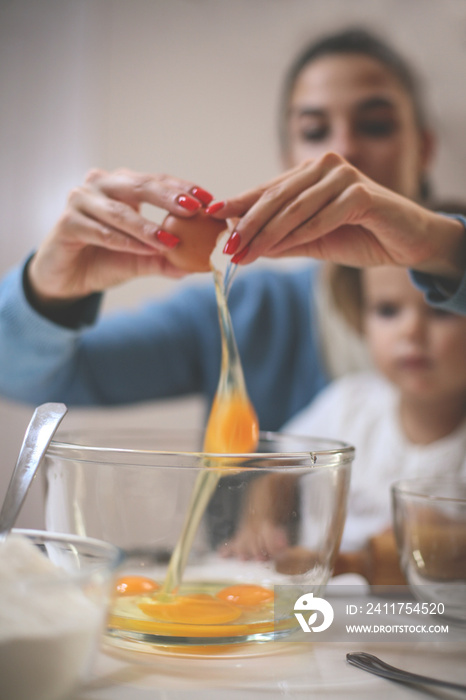 Mother and daughter together in kitchen baking cookie. Focus on foreground.