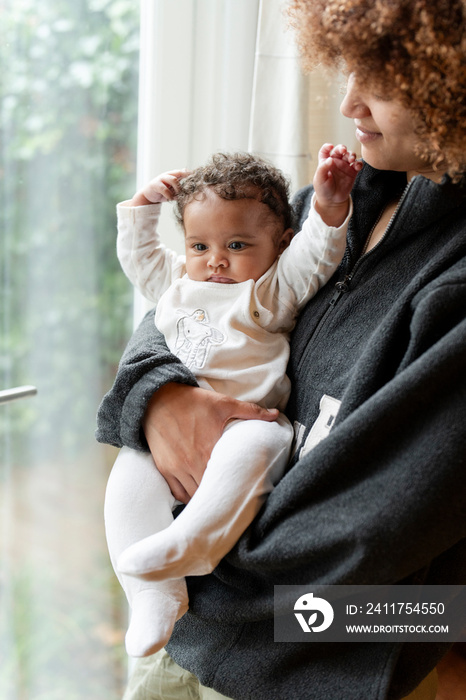 Mother holding baby daughter next to window