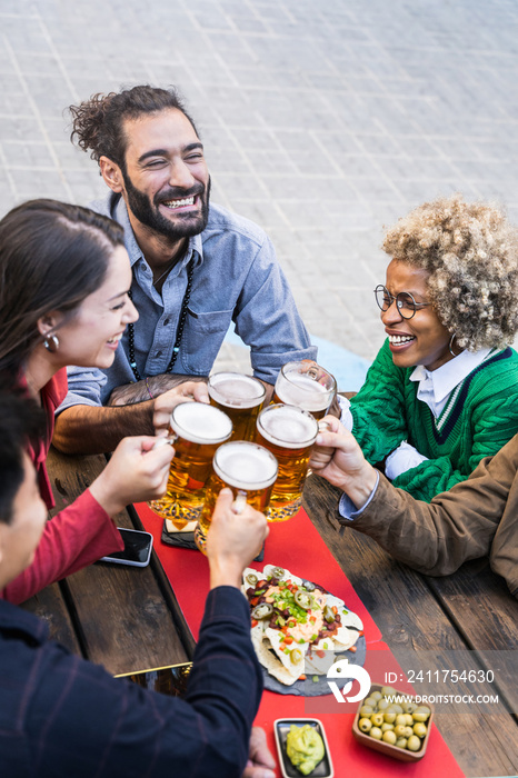 Group of happy multiethnic friends toasting beer mugs in a bar to celebrate friendship