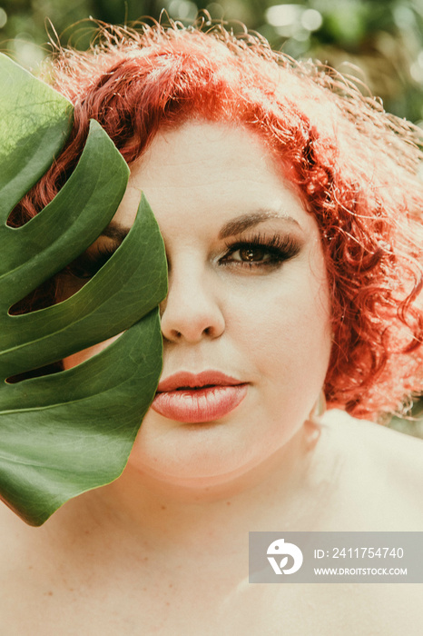 plus size red head holds leaf over facev