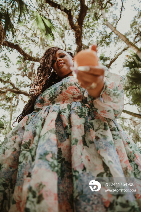 plus size Black woman looks down at camera holding orange