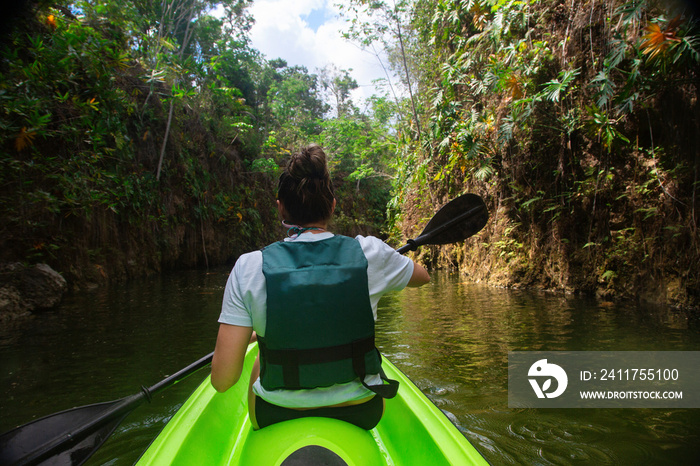 Woman kayaking along a beautiful tropical jungle river. Lots of copy space above and view from behind