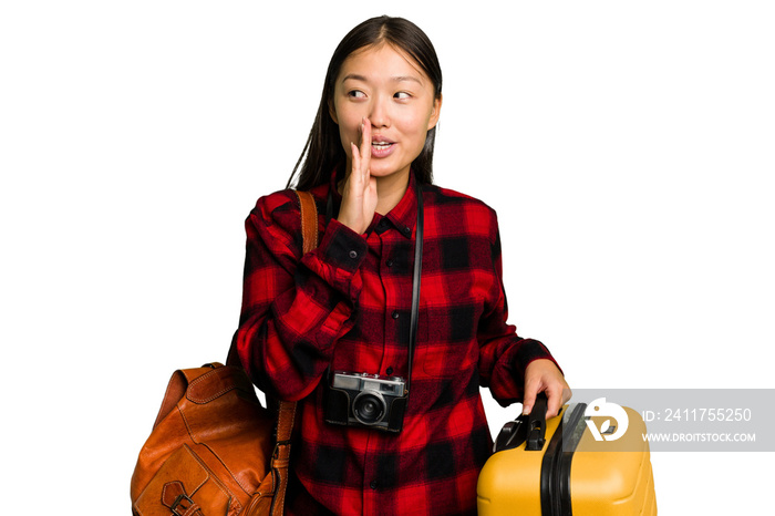 Traveler asian woman holding a suitcase isolated is saying a secret hot braking news and looking aside