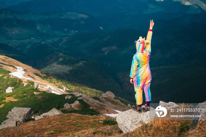 Female hiker in unicorn costume celebrating success in mountains