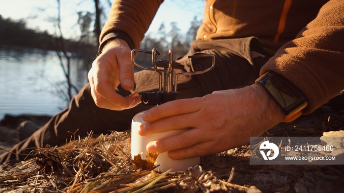 The theme of tourism is hiking and traveling in nature. Hands A Caucasian man uses equipping to cook food outside. A tourist installs a stove burner on a balloon cartridge with gas for boiling water