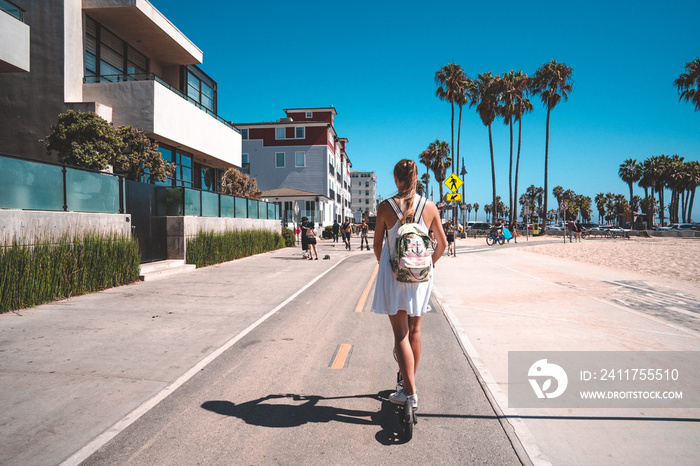 Beautiful girl riding an electric scooter down the Venice beach bike lane, along the beach and the Pacific ocean with an amazing view of California in LA. Electric scooter style.