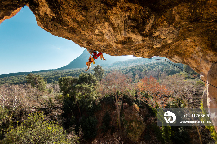 girl rock climber climbs a rock against the backdrop of a forest and blue mountains. rock climber resting on a difficult route. Rock climbing in Turkey.