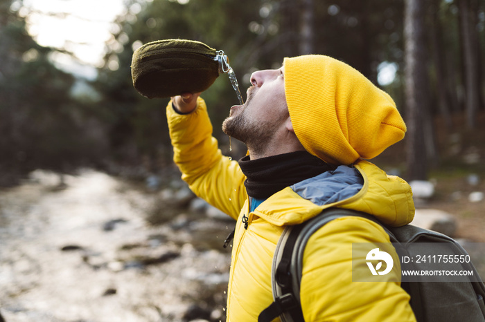 man in the forest drinks water from canteen