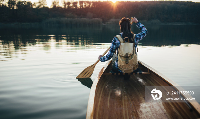 Travel girl paddling the canoe on the sunset lake