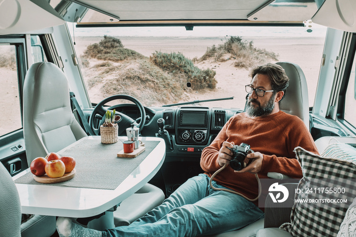One man sitting and relaxing inside a camper van motor home dinette. Vanlife lifestyle and travel modern people. Holiday vacation with van for alternative tourist and explorers. Beach view