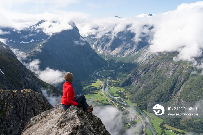 A woman hiker and traveller sitting on rock looking to mountains, Romsdalseggen trekking trail, Norway, Scandinavia