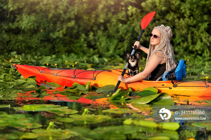 Beautiful young girl paddling in a kayak with a chihuahua dog through water lilies