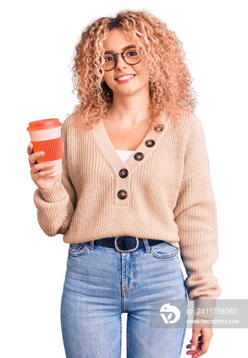 Young blonde woman with curly hair wearing glasses and drinking a cup of coffee looking positive and happy standing and smiling with a confident smile showing teeth