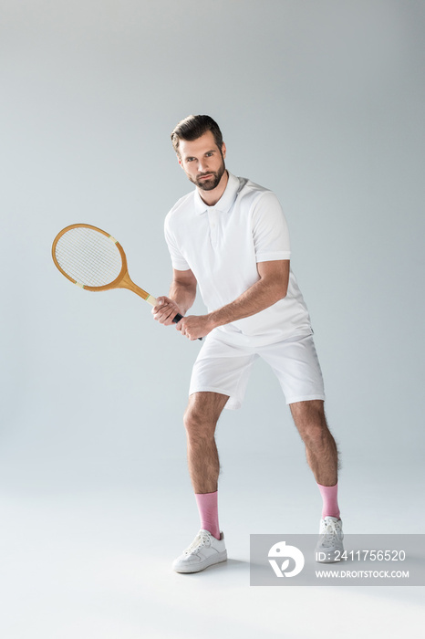 handsome tennis player with tennis racket looking at camera on grey