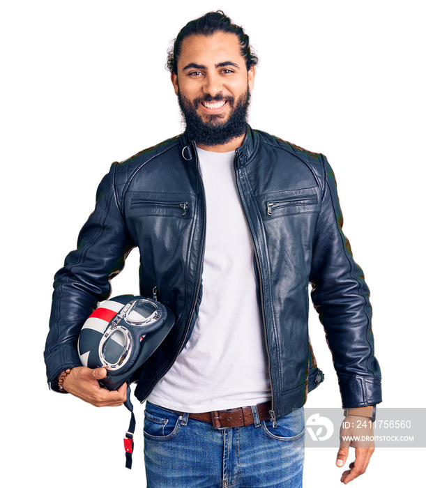 Young arab man holding motorcycle helmet looking positive and happy standing and smiling with a confident smile showing teeth