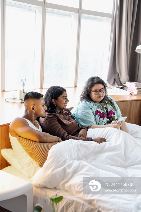 Three friends chatting and laughing together at home in bed