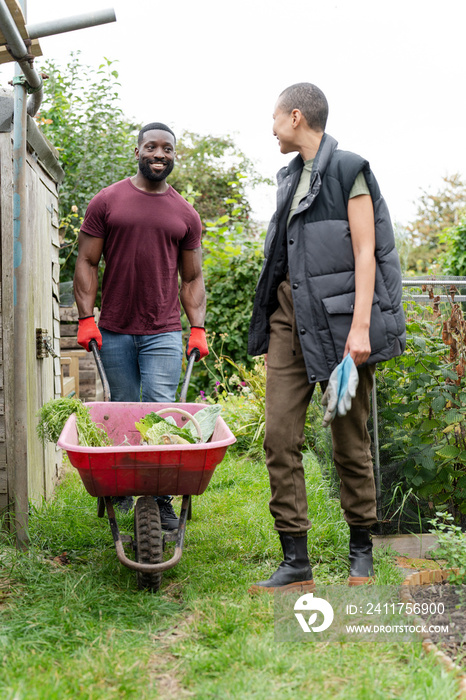 Smiling couple with vegetables in wheelbarrow in urban garden