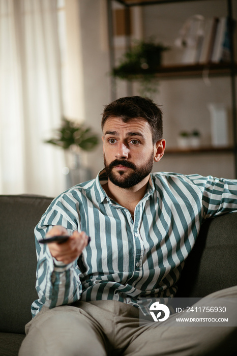 Young man at home. Man sitting in living room watching movie and drinking beer.