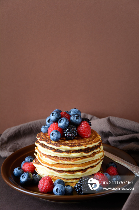 Stack of pancakes with fresh blueberry, raspberry and blackberry on brown plate