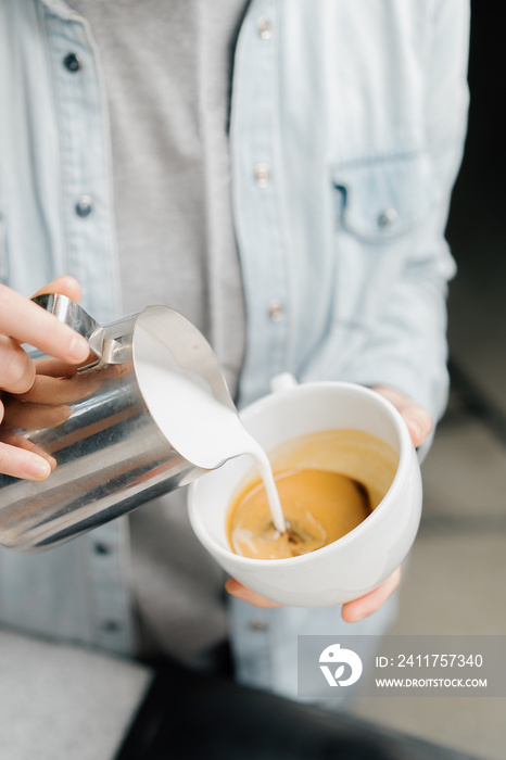 Barista making latte art in specialty coffee shop. Professional man making pouring stream milk with espresso