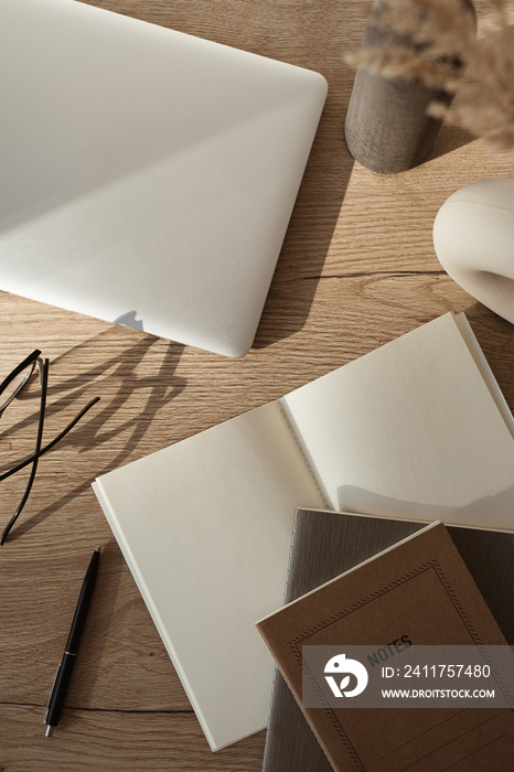 Home office desk workspace with laptop, notebook, glasses, sunlight shadows on neutral wooden background. Flat lay, top view blog, website, social media concept.