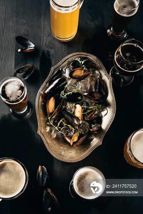 top view of arrangement of mugs of beer and mussels with ice cubes on dark wooden tabletop