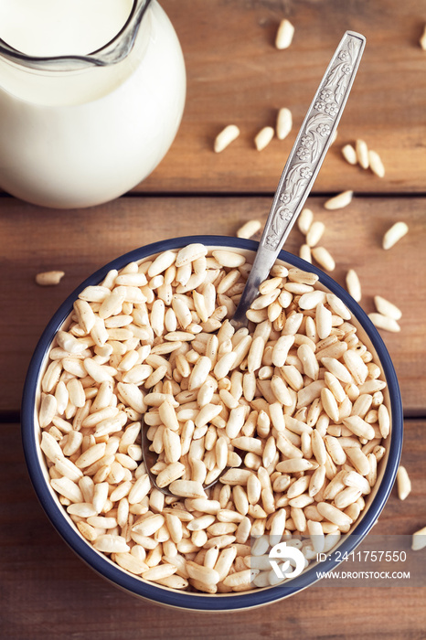 Puffed rice cereal in bowl with pitcher of milk on wooden background. Top view