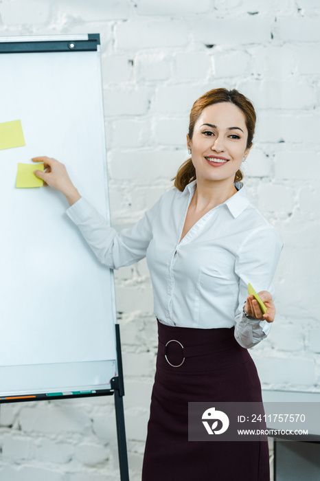 cheerful business coach putting sticky notes on white board