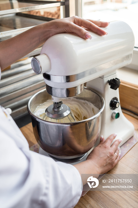 Close up of young woman using kitchen mixer preparing dough for sweet cake