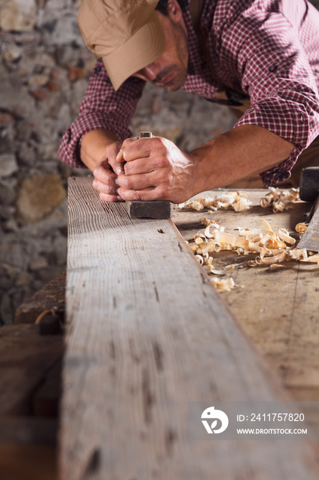 Carpenter smoothing out long wooden beam with tool