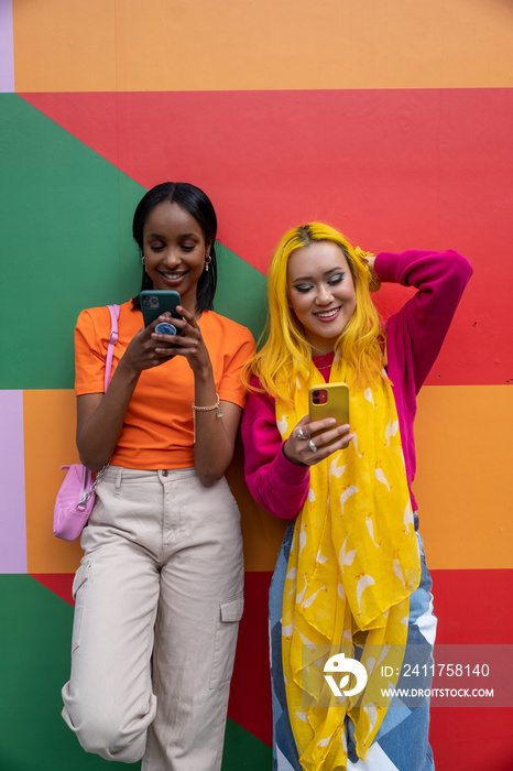 Young female friends using phones outdoors