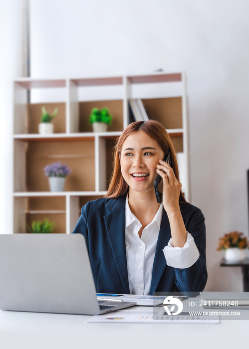 Successful Asian business woman smart using smart phone and laptop, mobile at working desk, feeling happy.