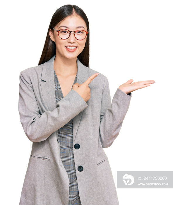 Young chinese woman wearing business clothes amazed and smiling to the camera while presenting with hand and pointing with finger.