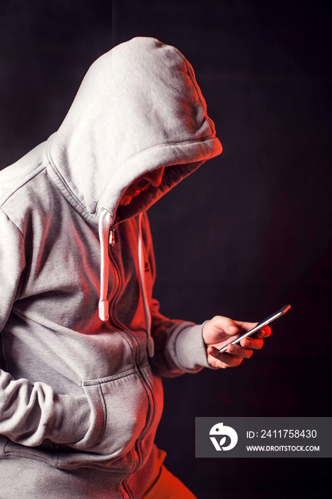 Man wearing hoody sweater with phone in hands. Crime and hacking concept