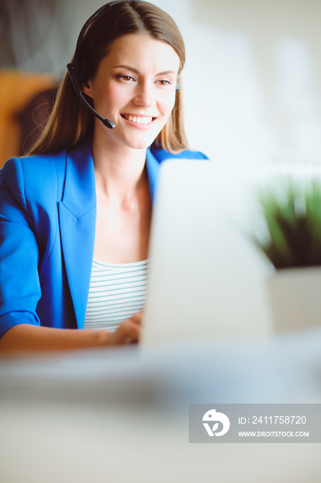 Portrait of beautiful business woman working at her desk with headset and laptop.