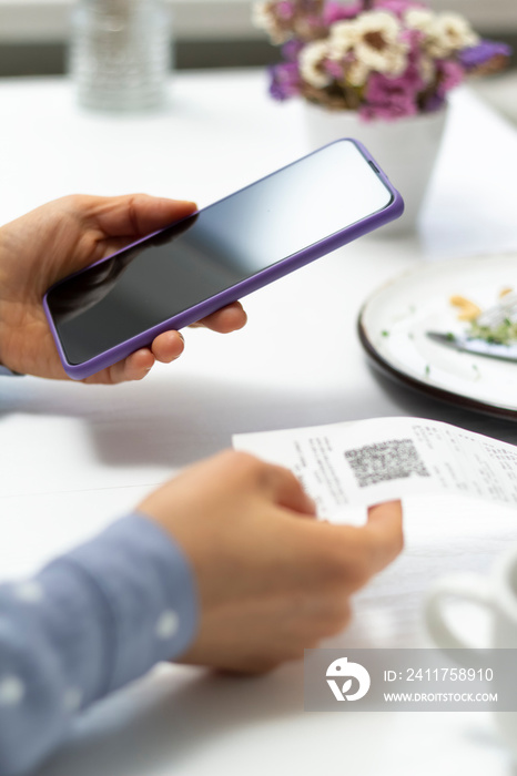 A woman scans a QR code using a phone in a cafe.