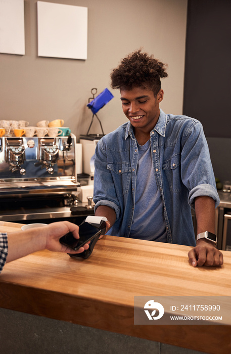 Barista holding reader and man paying by smartphone