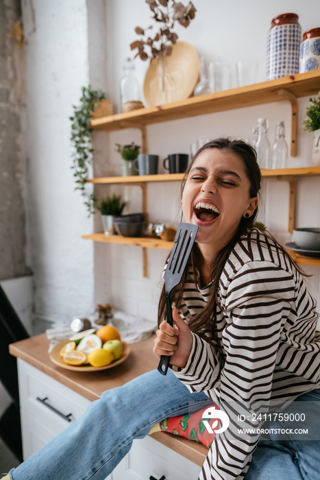 Funny woman singing into spatula, holding spatula as microphone.